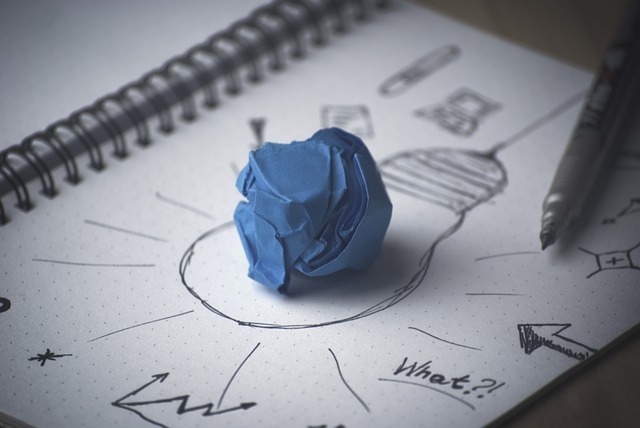 Image d'une boulette de papier bleu sur un cahier ouvert sur lequel est dessinée une ampoule