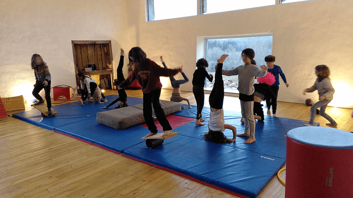 Photo du spectacle de fin de stage de cirque des enfants du groupe 8-14 ans. On voit des enfants faire du rola bola, le poirier, aidés par leurs camarades en parade, sur des tapis.